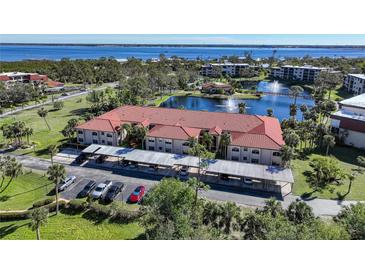 Beautiful aerial view of condo complex with red tile roof, lake, fountains, and waterfront views at 23465 Harborview Rd # 1006, Punta Gorda, FL 33980