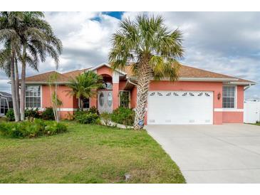 Charming coral home featuring a manicured lawn, palm trees, and a two-car garage at 126 Peckham Sw St, Port Charlotte, FL 33952