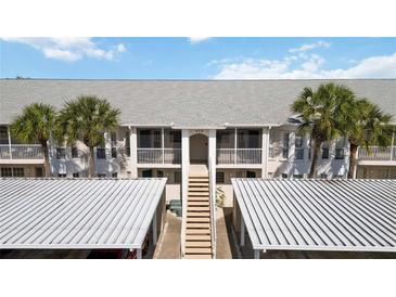 Exterior view of condominium building featuring palm trees, covered parking and second story entrance staircase at 432 Sunset Lake Blvd # 203, Venice, FL 34292