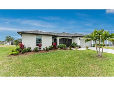 Landscaped front yard featuring a well-maintained lawn, colorful flowers, and a stately palm tree, complementing the home's architecture at 16265 Juarez Cir, Punta Gorda, FL 33955