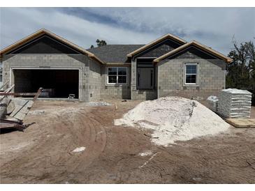 Unfinished gray home featuring an attached two car garage and neatly stacked construction materials in the front yard at 9590 Little Rock St, Port Charlotte, FL 33981