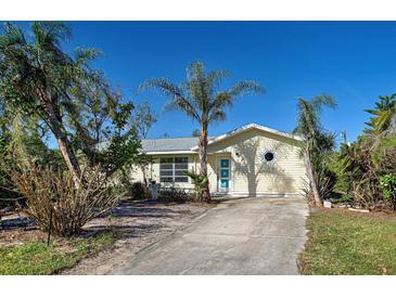 Charming single Gathering home with a yellow exterior, blue front door, palm trees, and concrete driveway at 7341 Hart St, Englewood, FL 34224