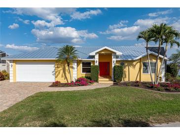 Charming single-story yellow home with a metal roof, a brick driveway, and lush landscaping at 258 Venezia Ct, Punta Gorda, FL 33950