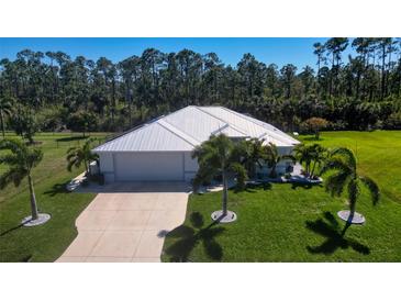 Stunning exterior elevation featuring a well-manicured lawn, metal roof, mature palms, and a concrete driveway at 25543 Prada Dr, Punta Gorda, FL 33955