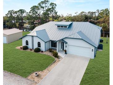 Beautiful single-story home featuring a well-manicured lawn, metal roof, arched entryway, and attached two-car garage at 908 Tropical Nw Cir, Port Charlotte, FL 33948
