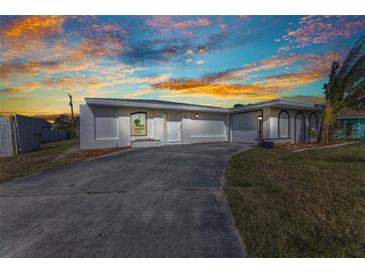 Single-story home featuring stucco walls, curved window accents, and a concrete driveway under a colorful sky at 3243 Elkcam Blvd, Port Charlotte, FL 33952