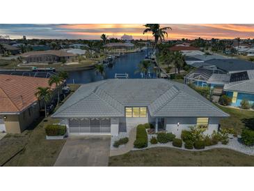 Waterfront home featuring a gray tile roof, screened garage, a concrete driveway, and mature landscaping at sunset at 2350 W Marion Ave, Punta Gorda, FL 33950