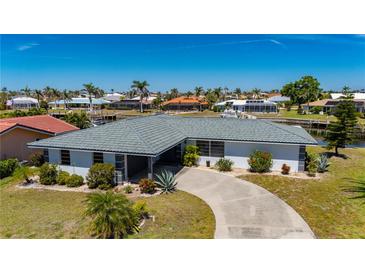 Waterfront home featuring mature landscaping, tile roof, and circular driveway surrounded by lush tropical foliage at 1206 Winward Ct, Punta Gorda, FL 33950