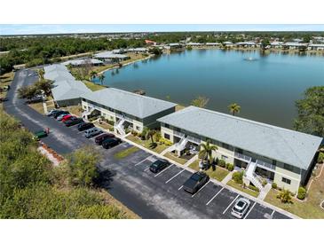 Aerial view of a two-story condo complex with ample parking overlooking a scenic lake and fountain at 25225 Rampart Blvd # 205, Punta Gorda, FL 33983