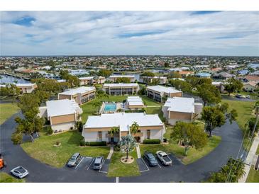 Wide aerial view of condos with central pool, circular drive, and ample parking in a residential neighborhood at 1080 Bal Harbor Blvd # 10C, Punta Gorda, FL 33950