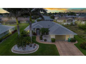 Beautiful single-story home featuring lush landscaping, palm trees, and a brick driveway at 23104 Turnbull Ave, Port Charlotte, FL 33954