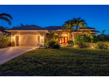 Beautiful home at dusk, featuring a lush lawn, tropical landscaping, and a vibrant red front door at 211 Lido Dr, Punta Gorda, FL 33950