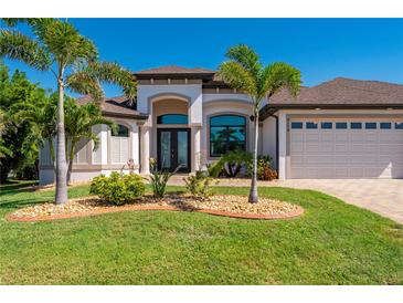 Well-manicured home featuring a three-car garage, tropical landscaping, and a paver driveway at 4174 Perch Cir, Port Charlotte, FL 33948