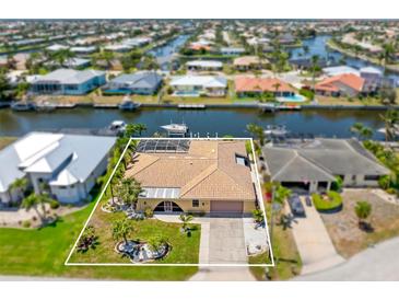 Waterfront home featuring lush landscaping, a tile roof, and a screened-in pool, located on a canal with boat dock at 931 Cimarron Dr, Punta Gorda, FL 33950