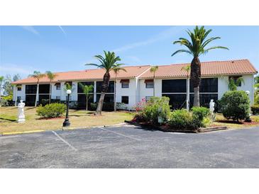 Condominium building featuring a red tile roof and white exterior with mature tropical landscaping and a paved parking lot at 2275 S Mccall Rd # 103, Englewood, FL 34224