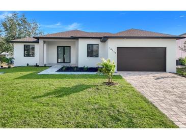 Inviting single-story home with a well-manicured lawn, stylish landscaping, and a paved driveway leading to an attached garage at 1 Goldenrod Dr, Placida, FL 33946