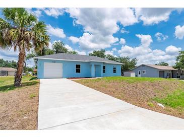 Charming single-story blue home featuring an attached garage and a well-manicured lawn at 21480 Eldred Ave, Port Charlotte, FL 33952