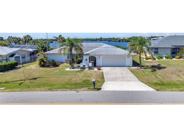 Inviting single-story home with a well-manicured lawn, palm trees, and a long driveway leading to an attached garage at 318 Spring Lake Nw Blvd, Port Charlotte, FL 33952