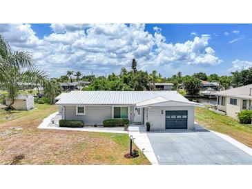 Beautiful one-story home featuring a manicured lawn, grey exterior, and a pristine white metal roof at 27385 Voyageur Dr, Punta Gorda, FL 33983