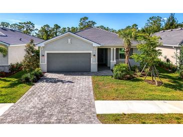Charming single-story home with a well-manicured lawn, paver driveway, and gray tiled roof at 10995 Pinot Dr, Venice, FL 34293