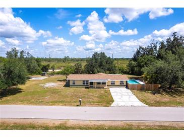 Ranch-style home with a pool, front porch, long driveway, and large yard under a cloudy blue sky at 30154 Beech Rd, Punta Gorda, FL 33982