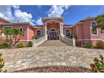 Grand pink two-story home with a paver driveway, manicured landscaping, and an elegant front entrance with a stone staircase at 4409 Crews Ct, Port Charlotte, FL 33952