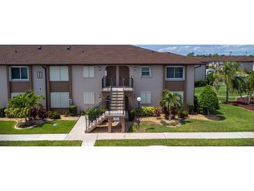 A tan condo with brown accents shows stairs to the second floor entrance, and beautifully landscaped grounds at 25100 Sandhill Blvd # I-204, Punta Gorda, FL 33983