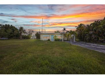 Charming single-story home featuring a large grassy lawn with tropical trees at a colorful sunset at 426 Burland St, Punta Gorda, FL 33950