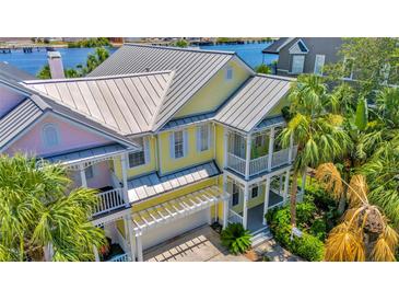 Inviting yellow two-story home with metal roof, dual balconies, lush tropical landscaping, and pergola-covered driveway at 936 Hemingway Cir, Tampa, FL 33602