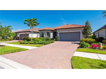 Charming single-story home with a red tile roof, brick driveway, lush landscaping, and a two-car garage at 1470 Hyssop Loop, North Port, FL 34289