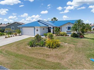 Single-story home showcasing a bright blue metal roof, lush landscaping, and a well-manicured lawn at 3825 Barnegat Dr, Punta Gorda, FL 33950