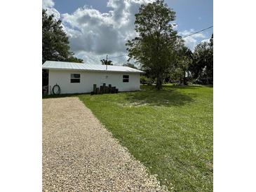 Charming white home featuring a metal roof, gravel driveway, and spacious green yard at 5727 Beechwood St, Punta Gorda, FL 33982