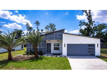 Modern home featuring a gray and white exterior, manicured lawn, palm trees and a two car garage at 14174 Packard Ave, Port Charlotte, FL 33953