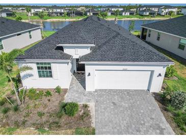 Aerial view of a well-maintained home with a gray roof, paver driveway, lake view, and manicured landscaping at 15069 Anchorage Rd, Punta Gorda, FL 33982