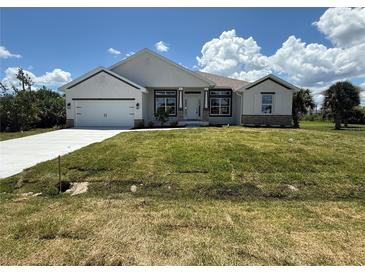 Charming single-story home featuring a lush green lawn, a two car garage, and a beautifully landscaped front yard at 9469 Spring Cir, Port Charlotte, FL 33981