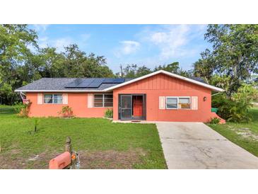 Charming coral-colored home featuring a well-manicured lawn, solar panels, and a concrete driveway at 2031 Backton St, Port Charlotte, FL 33948