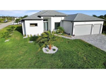Landscaped front yard featuring lush grass, palm trees, and a modern white house with a gray roof at 13406 Chenille Dr, Port Charlotte, FL 33981