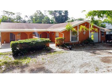Inviting one-story home features an orange exterior, manicured shrubs, and a gravel driveway at 2131 Heasley Rd, Englewood, FL 34223
