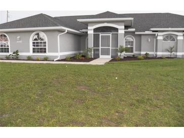 Charming single-story home featuring a well-manicured lawn, arched windows, and a screened-in entryway at 23167 Turnbull Ave, Port Charlotte, FL 33954