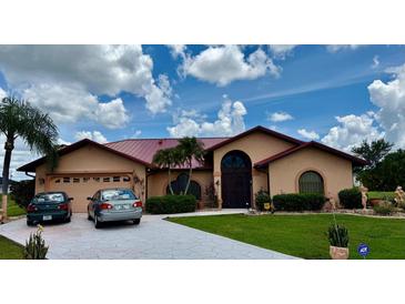 Inviting single-story home featuring a metal roof, arched windows, lush landscaping, and a spacious driveway at 214 Castile Ct, Punta Gorda, FL 33983