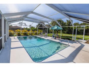 Beautiful screened-in pool with lounge seating, umbrella table and lush landscaping at 3270 Ithaca St, Port Charlotte, FL 33952