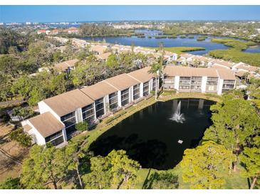 Scenic aerial view of the condo complex with a pond and fountain amidst lush greenery, showcasing waterfront living at 1144 Bird Bay Way # 102, Venice, FL 34285