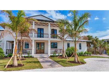 Elegant two-story home featuring a charming front porch, wooden accents, and lush landscaping with mature palm trees at 10009 Gasparilla Pass Blvd, Boca Grande, FL 33921