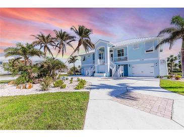 Two-story light blue house with a metal roof, palm trees, and landscaped yard at 13104 Via Cassia, Placida, FL 33946