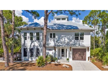 Two-story home with a metal roof, white siding, inviting entryway, and attached garage on a sunny day at 7064 Baypine Ln, Englewood, FL 34224