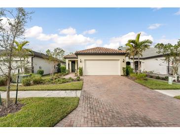 Brick paved driveway leads to a beige house with a white garage door and landscaped front yard at 2759 Lavandula Ct, North Port, FL 34289