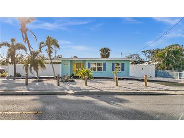 Charming waterfront home with vibrant blue exterior, tropical landscaping, and white picket fence under a clear blue sky at 539 Shore Rd, Nokomis, FL 34275