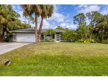 Charming home featuring a two-car garage, a well-manicured lawn, and lush tropical landscaping at 2700 Colonade Ln, North Port, FL 34286