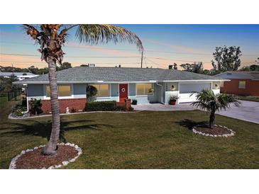 Charming single-story home with a well-manicured lawn, red front door, palm trees, and an attached two-car garage at 1690 Edith Ave, Englewood, FL 34223