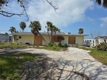 Exterior view of a yellow single-story home with boarded windows and a sandy yard with palm trees at 1432 Lemon Bay Dr, Englewood, FL 34223